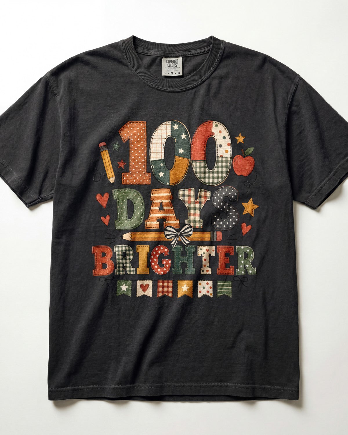 Black Comfort Colors short-sleeve graphic t-shirt laid flat against a white background. The front features a colorful patchwork-style graphic reading '100 DAYS BRIGHTER' with school-themed illustrations like stars, hearts, and pencils.