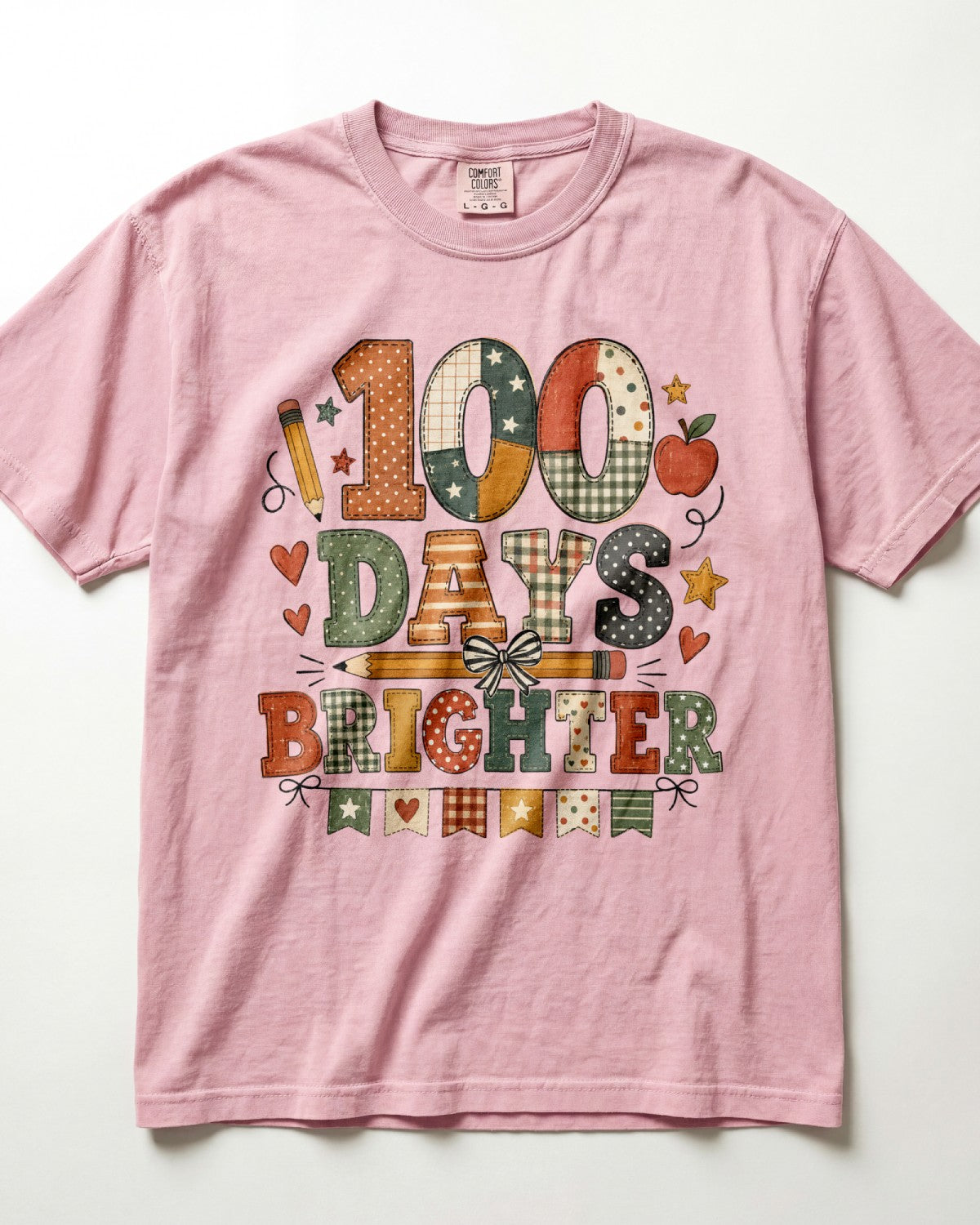 Blossom Comfort Colors short-sleeve crewneck t-shirt featuring a colorful graphic print on the front that reads '100 DAYS BRIGHTER' in patchwork-style letters with autumn motifs like stars, hearts, and an apple.