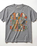 grey Comfort Colors short-sleeve t-shirt featuring a colorful graphic print that reads '100 DAYS BRIGHTER' in patchwork-style letters with autumn and school motifs like stars, hearts, pencils, and apples.