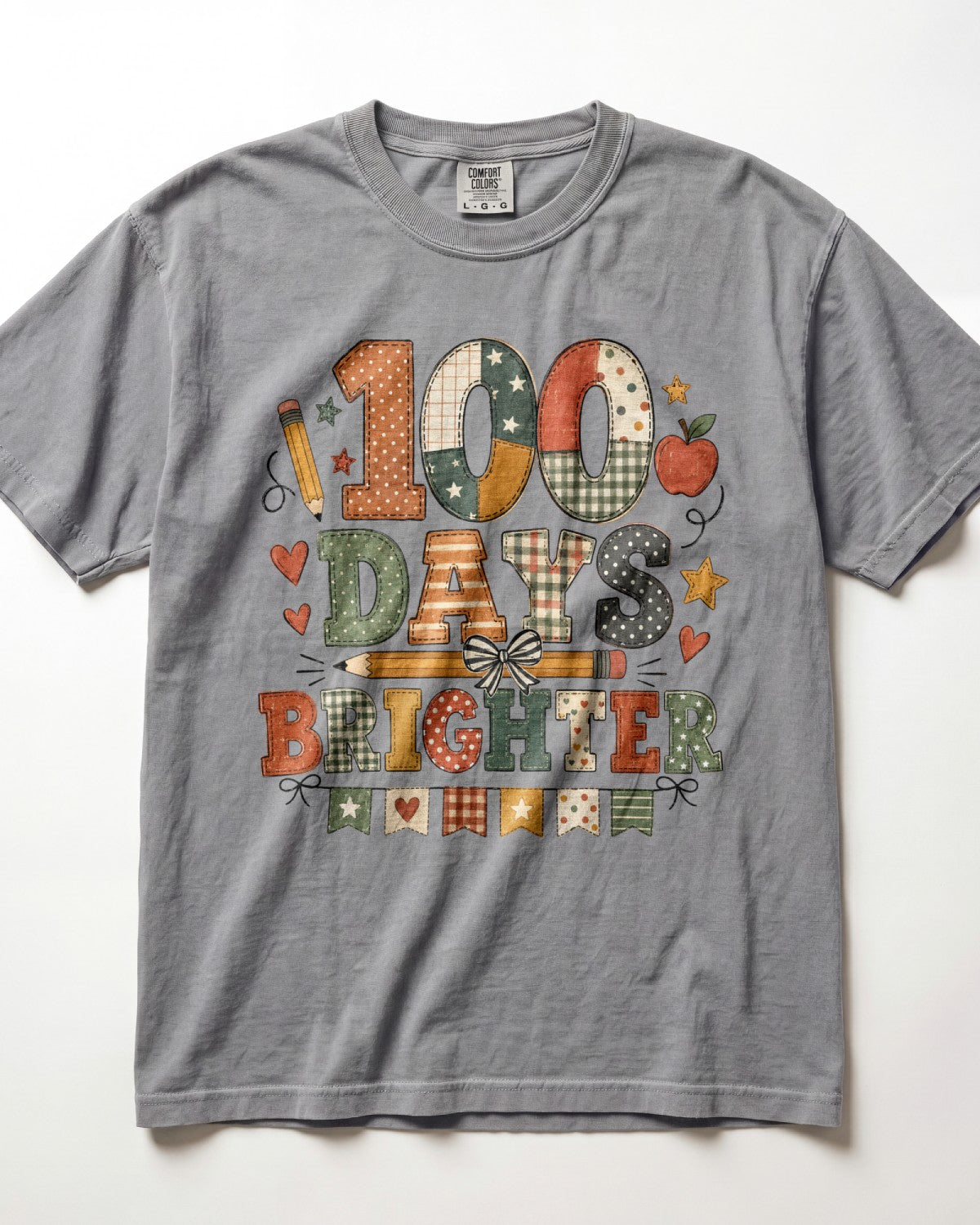 grey Comfort Colors short-sleeve t-shirt featuring a colorful graphic print that reads '100 DAYS BRIGHTER' in patchwork-style letters with autumn and school motifs like stars, hearts, pencils, and apples.