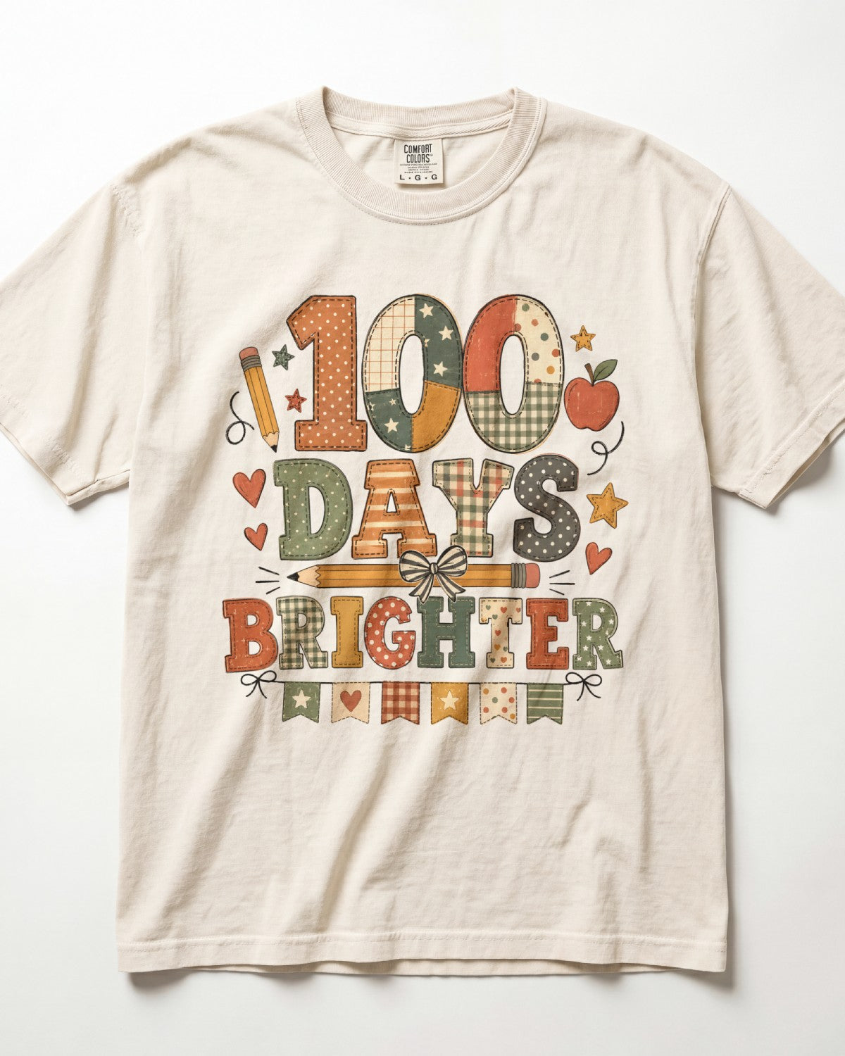 Ivory Comfort Colors short-sleeve t-shirt with a colorful graphic on the front that reads '100 DAYS BRIGHTER' in patchwork-style letters, decorated with stars, hearts, pencils, and an apple.