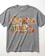 Light gray crew-neck short-sleeve T-shirt with “Kindergarten Teacher” fall graphic print