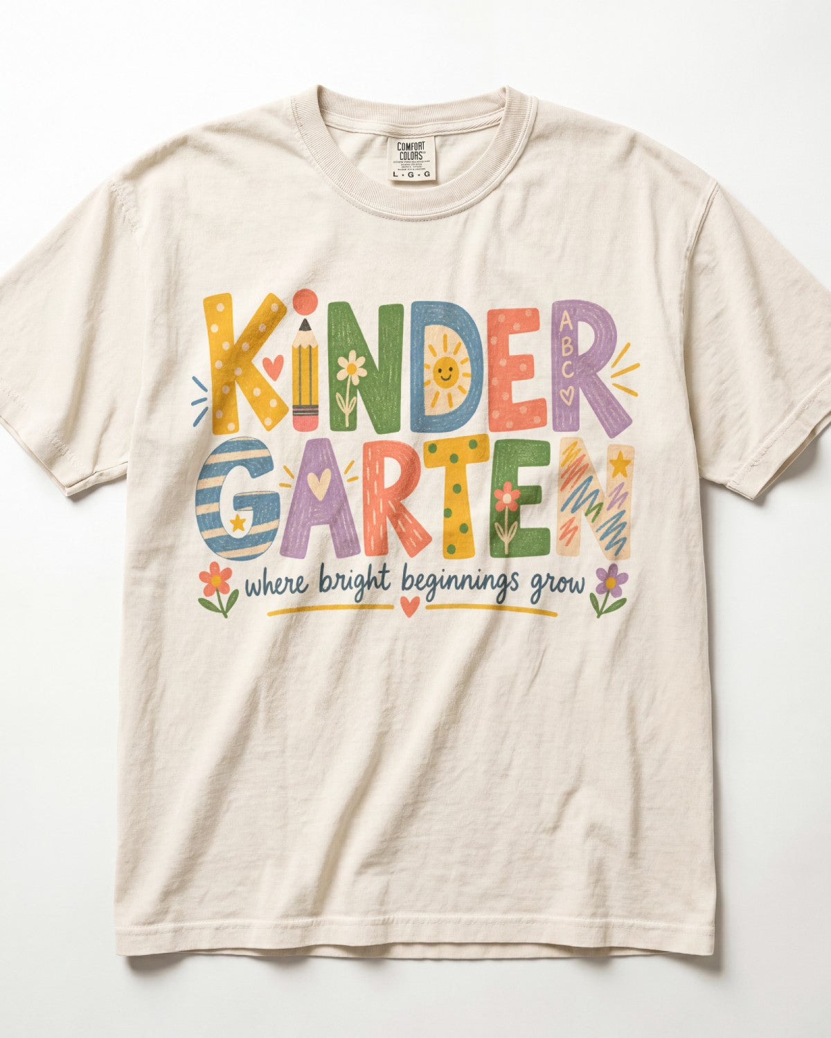 An ivory t-shirt with colorful text that says "KINDER GARTEN" and "where bright beginnings grow".