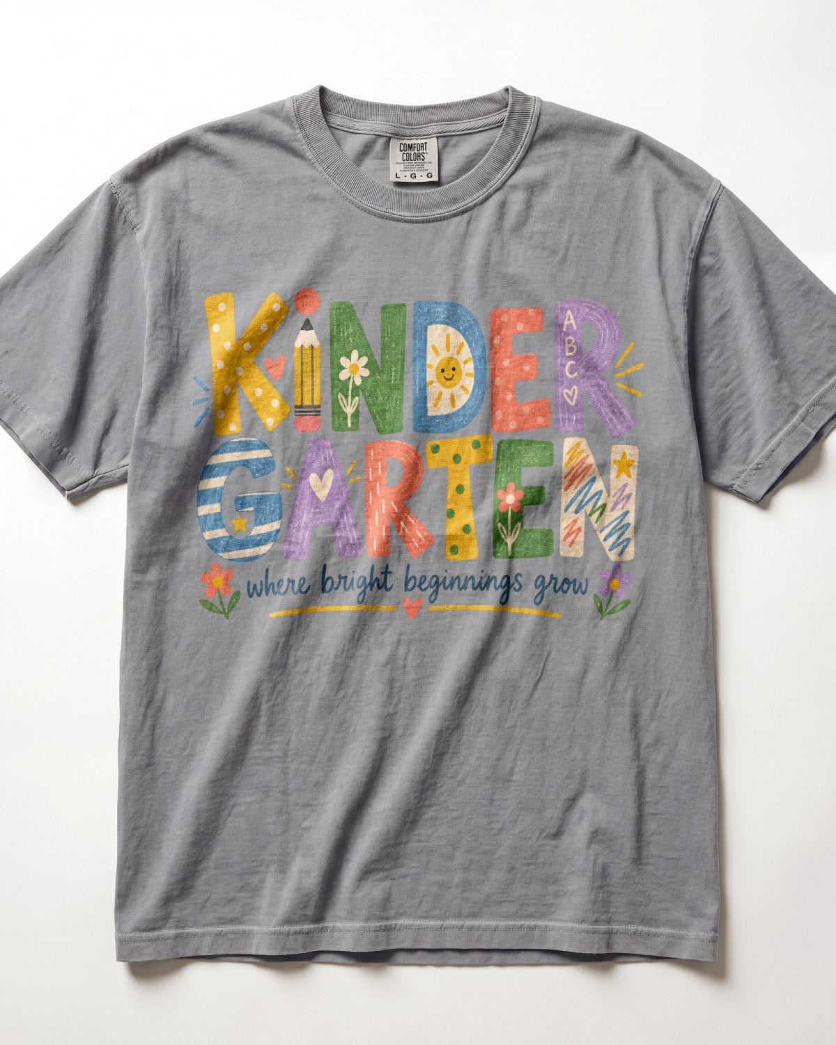 A gray t-shirt with colorful text that says "KINDERGARTEN" and "where bright beginnings grow".