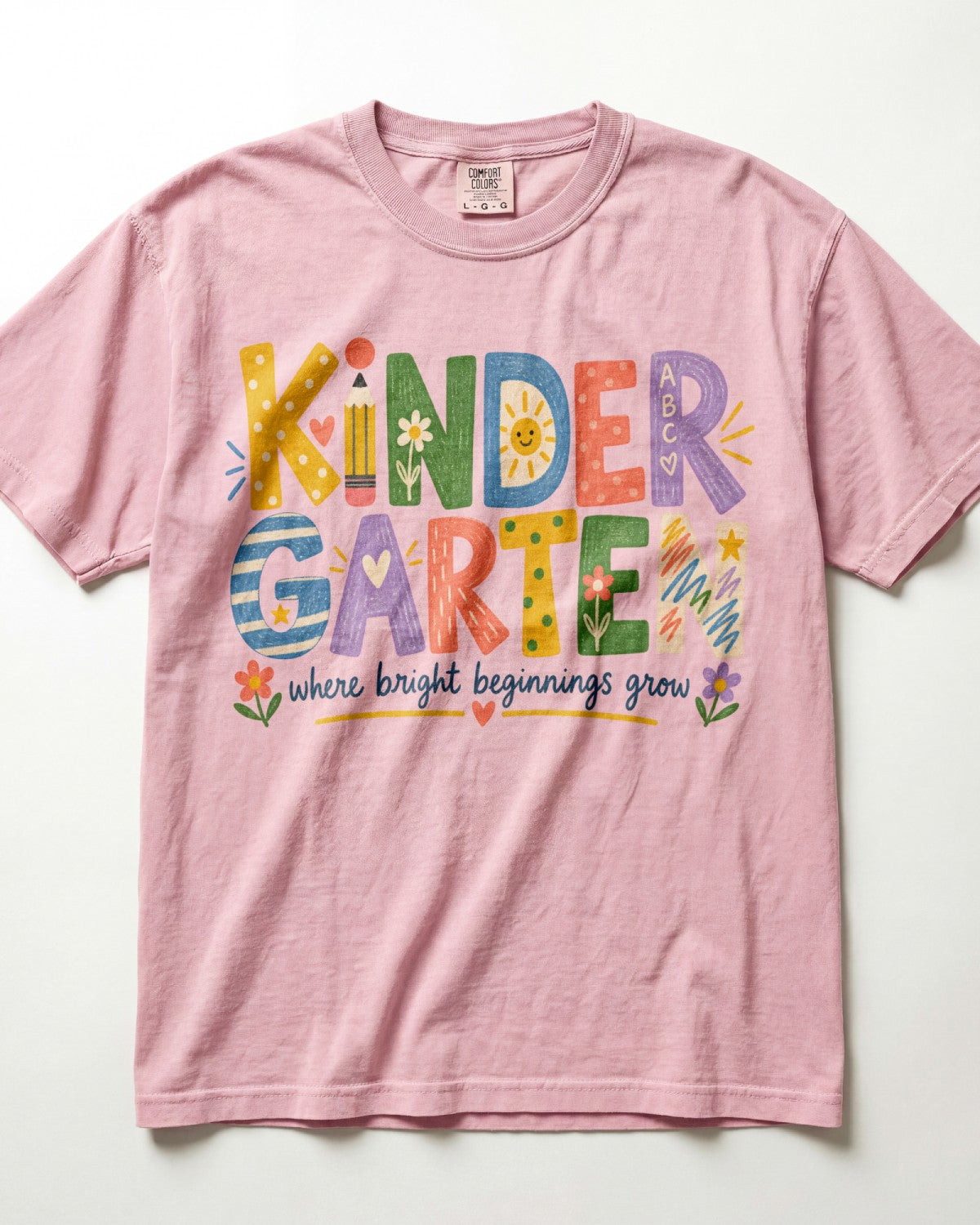 A pink/blossom t-shirt with the text "KINDER GARTEN" and colorful illustrations, along with the text "where bright beginnings grow" printed on it.