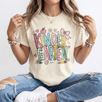 Cream kindergarten teacher T-shirt worn by model with “Kinder Garden” graphic and hearts