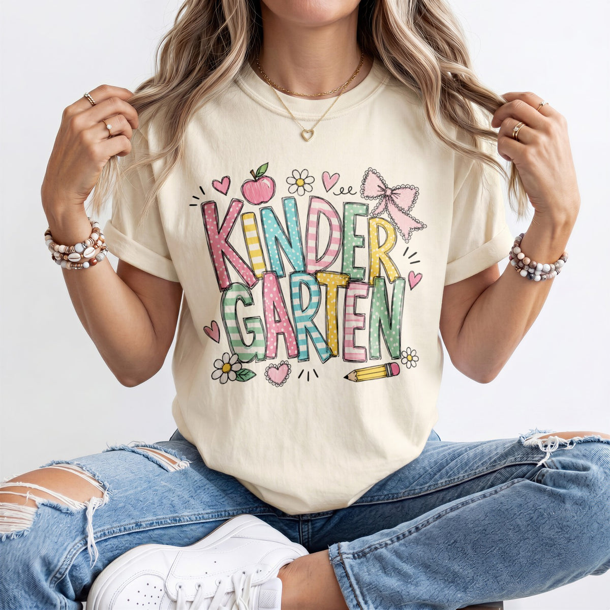 Cream kindergarten teacher T-shirt worn by model with “Kinder Garden” graphic and hearts