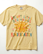 Butter Comfort Colors kindergarten teacher shirt featuring a colorful sun graphic and “Bright Little Beginnings” text, displayed in a flat lay.