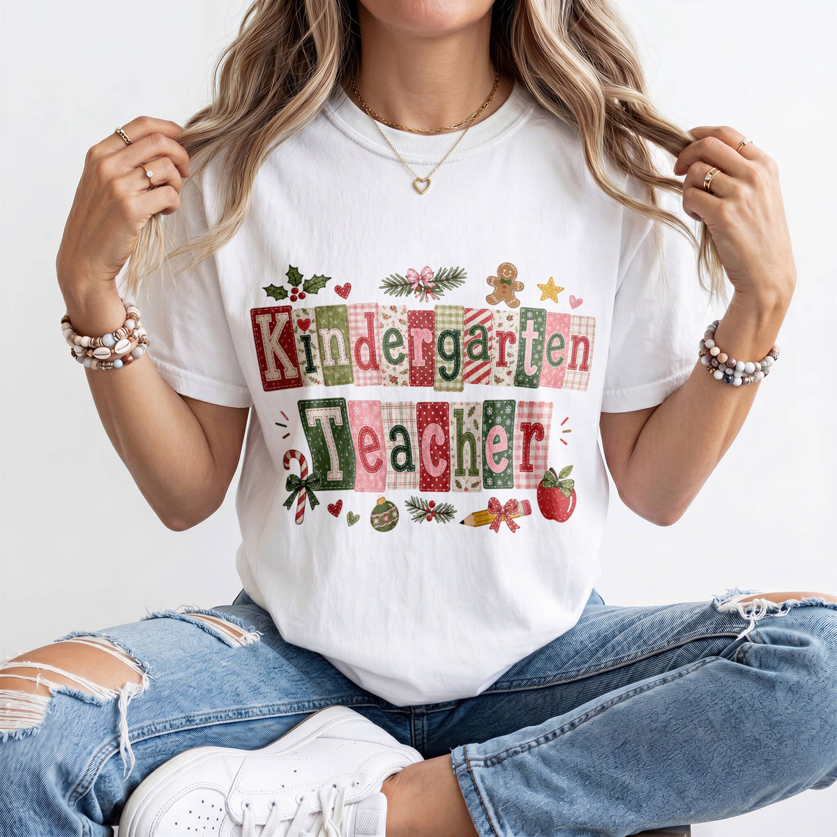 A woman wearing a white t-shirt with the text "Kindergarten Teacher" and various holiday-themed graphics, including a gingerbread man, holly leaves, and a star.