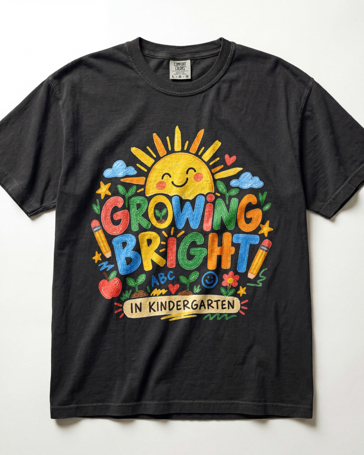 A black short-sleeve t-shirt with a colorful graphic on the front that reads 'GROWING BRIGHT IN KINDERGARTEN' with a smiling sun, clouds, stars, and school-themed icons.