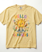 A pale yellow/butter short-sleeve t-shirt with a colorful cartoon sun graphic and the text 'HELLO LITTLE LEARNERS' on the front, displayed flat against a white background.