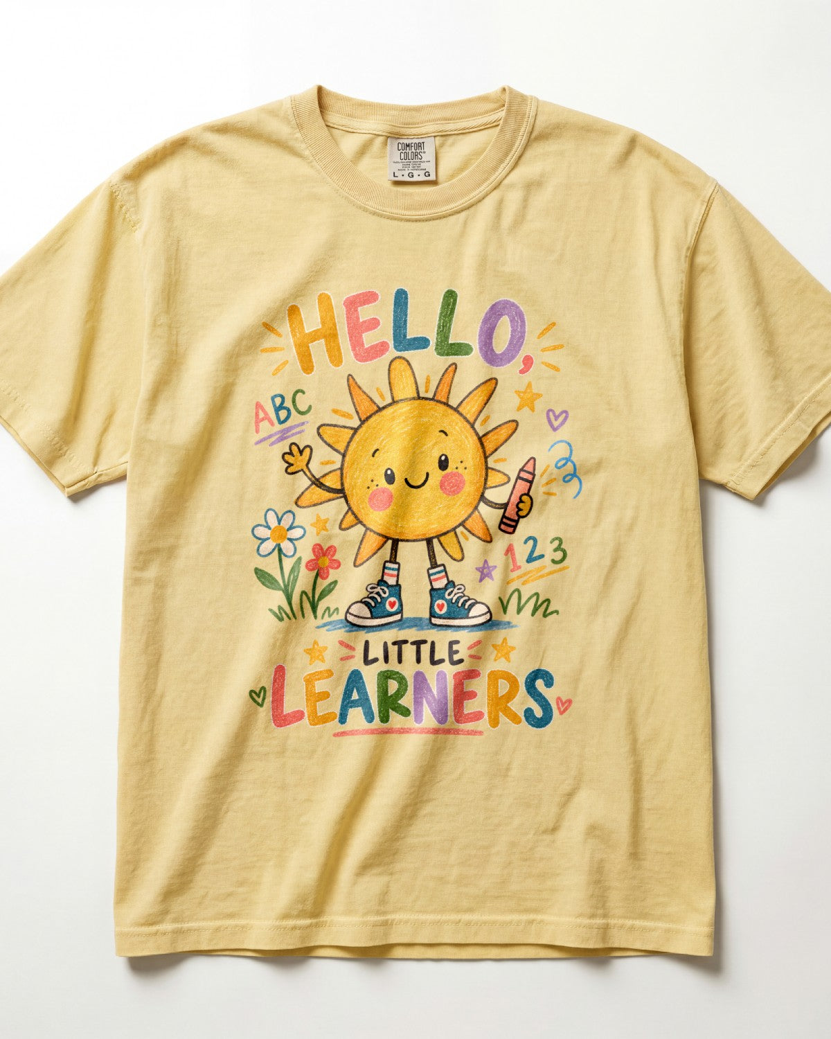A pale yellow/butter short-sleeve t-shirt with a colorful cartoon sun graphic and the text 'HELLO LITTLE LEARNERS' on the front, displayed flat against a white background.