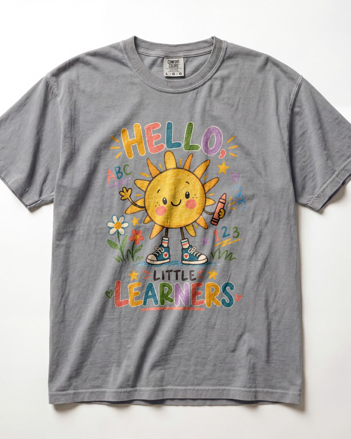 A grey short-sleeve t-shirt with a colorful graphic of a smiling sun character and the text 'HELLO! LITTLE LEARNERS' on the front, displayed flat against a white background.