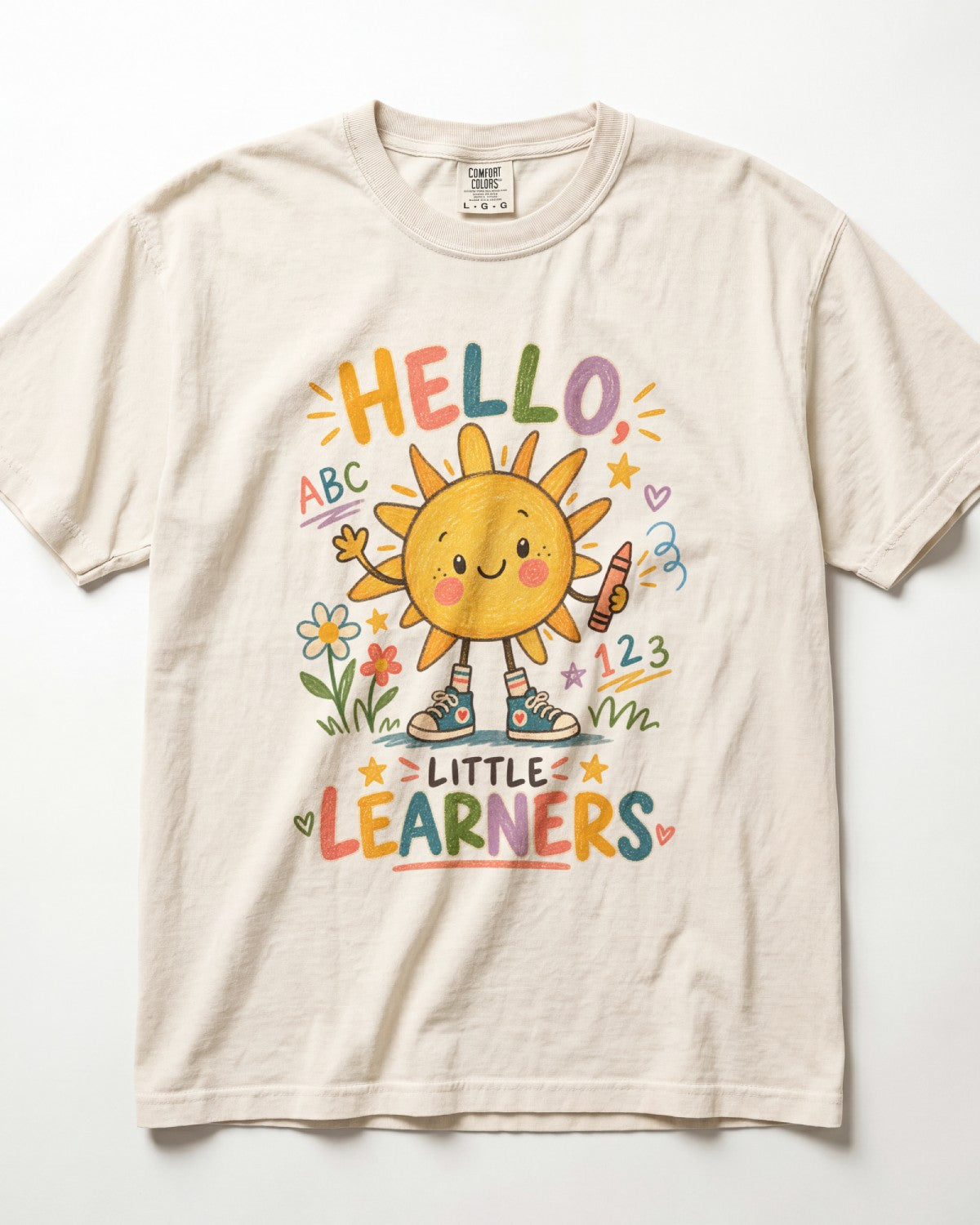 A cream-colored/ivory short-sleeve t-shirt with a colorful graphic of a smiling sun and the text 'HELLO, LITTLE LEARNERS' on the front, displayed flat against a white background.