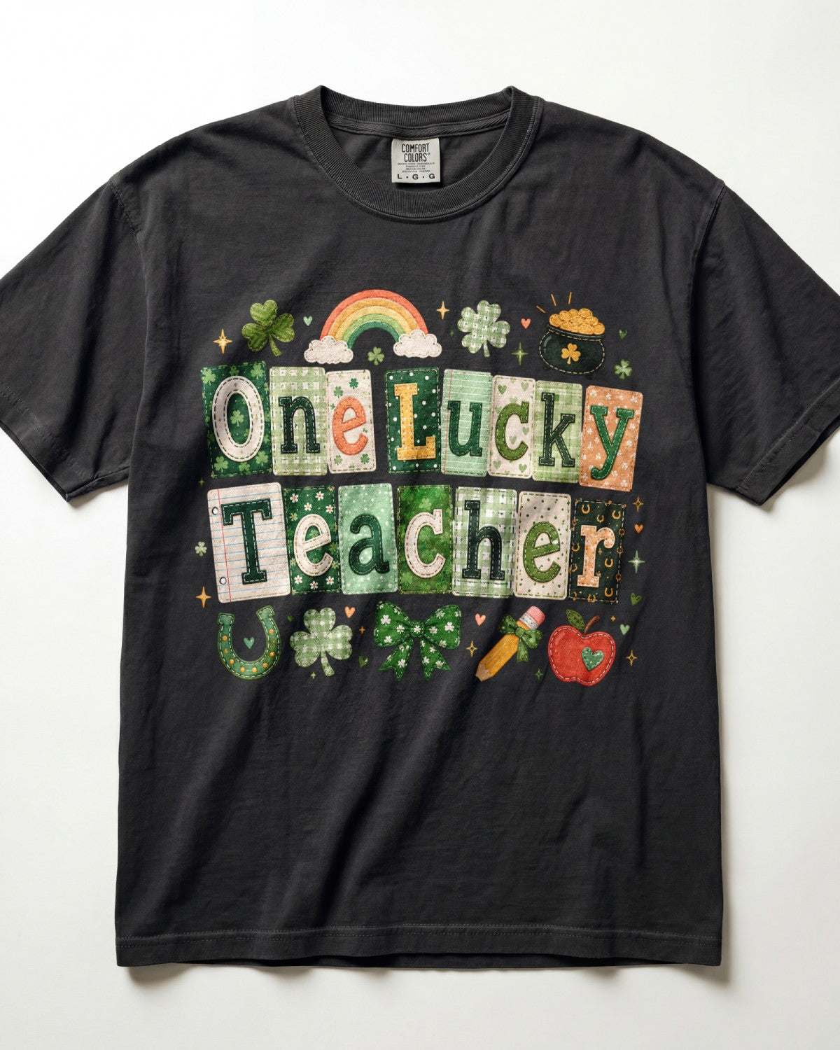 A black short-sleeve crewneck t-shirt featuring a colorful graphic that reads 'One Lucky Teacher' in St. Patrick's Day themed tiles, decorated with shamrocks, a rainbow, a pot of gold, a horseshoe, and an apple, laid flat against a white background.