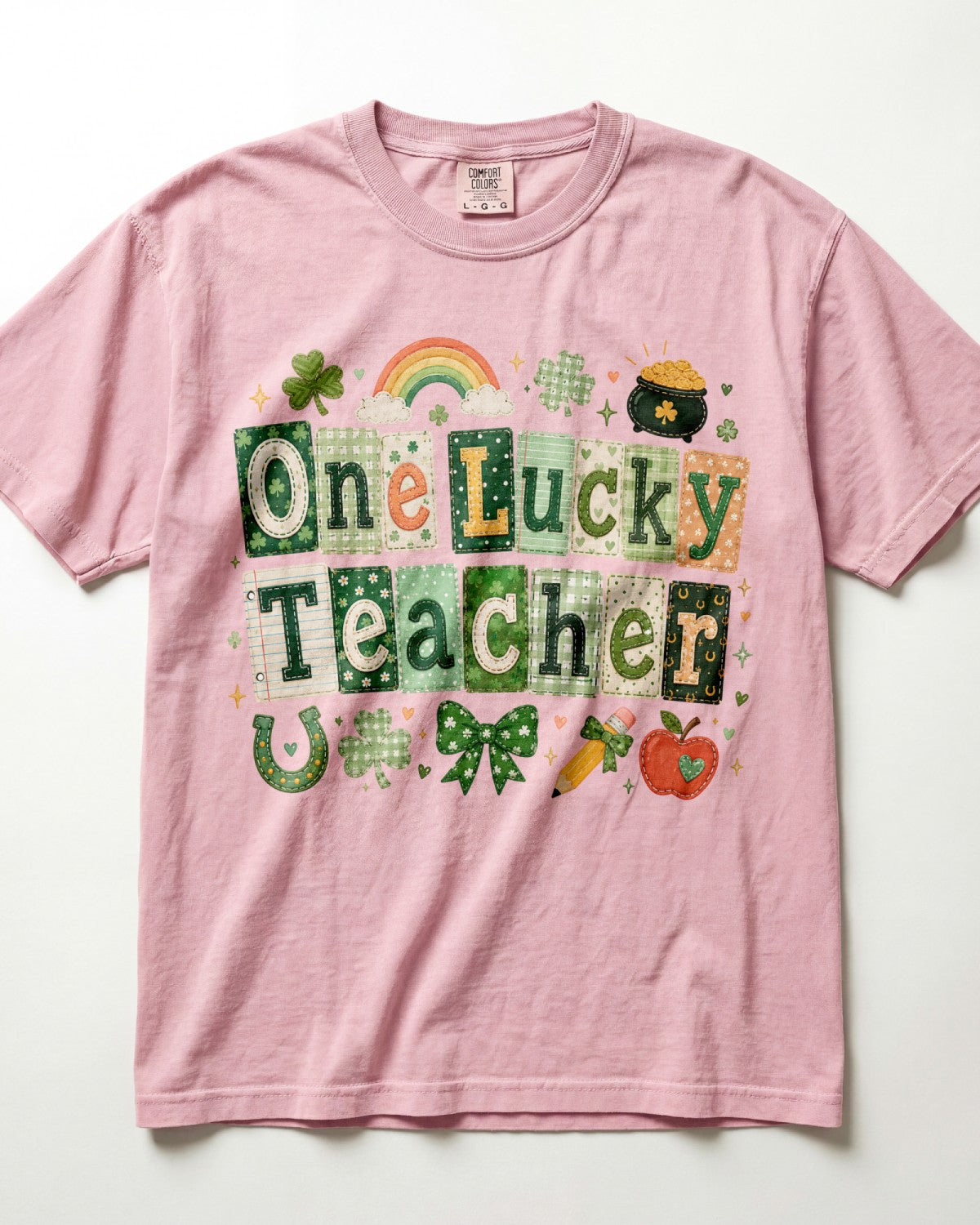 A blossom short-sleeve crewneck t-shirt featuring a St. Patrick's Day graphic that reads 'One Lucky Teacher' in green patchwork-style letters, decorated with a rainbow, shamrock, leprechaun pot, and other festive motifs.