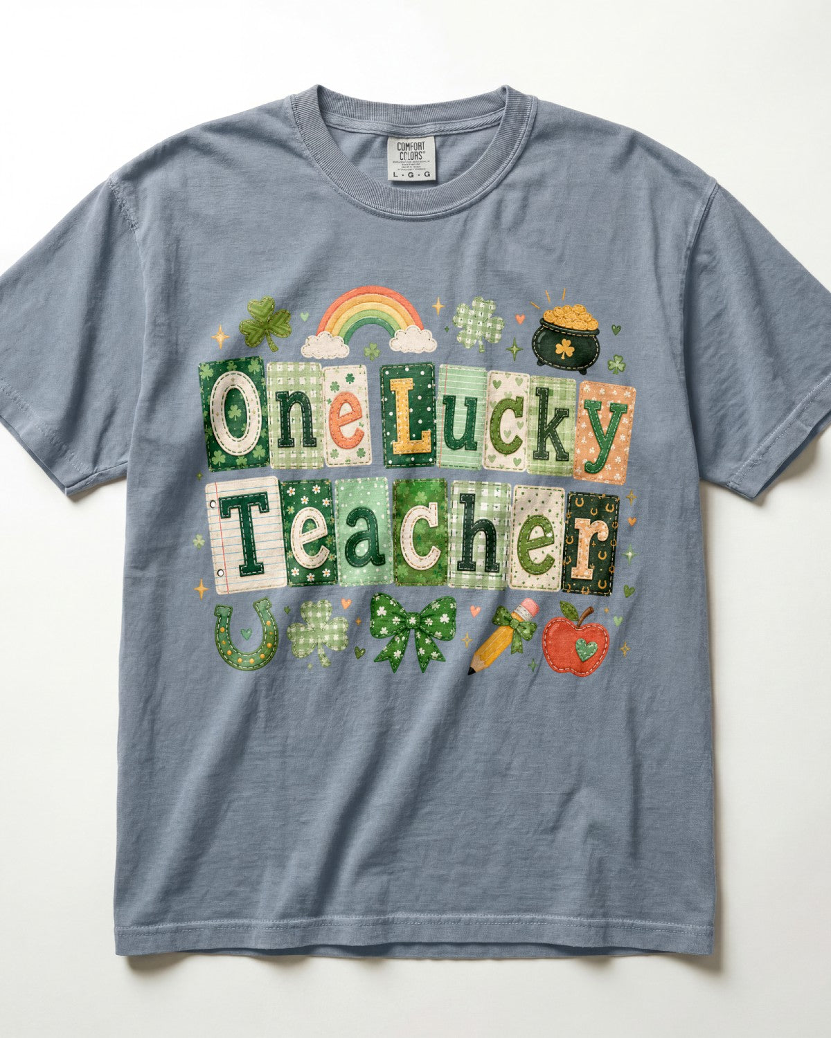 A heathered slate blue/blue jean short-sleeve t-shirt featuring a St. Patrick's Day graphic that reads 'One Lucky Teacher' in patchwork-style green and beige letters, decorated with a rainbow, clover, shamrock, pot of gold, horseshoe, bow, pencil, and apple on a white background.