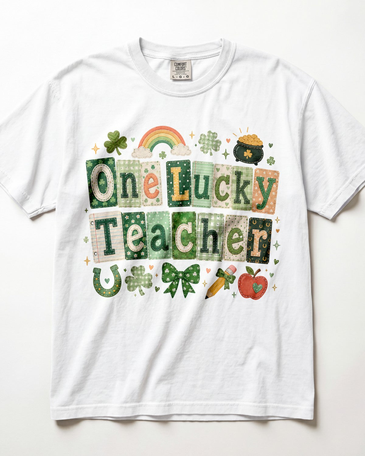 A white short-sleeve crewneck t-shirt featuring a St. Patrick's Day graphic that reads 'One Lucky Teacher' in a patchwork pattern of green, white, and orange squares, decorated with a rainbow, shamrocks, a pot of gold, and a carrot.