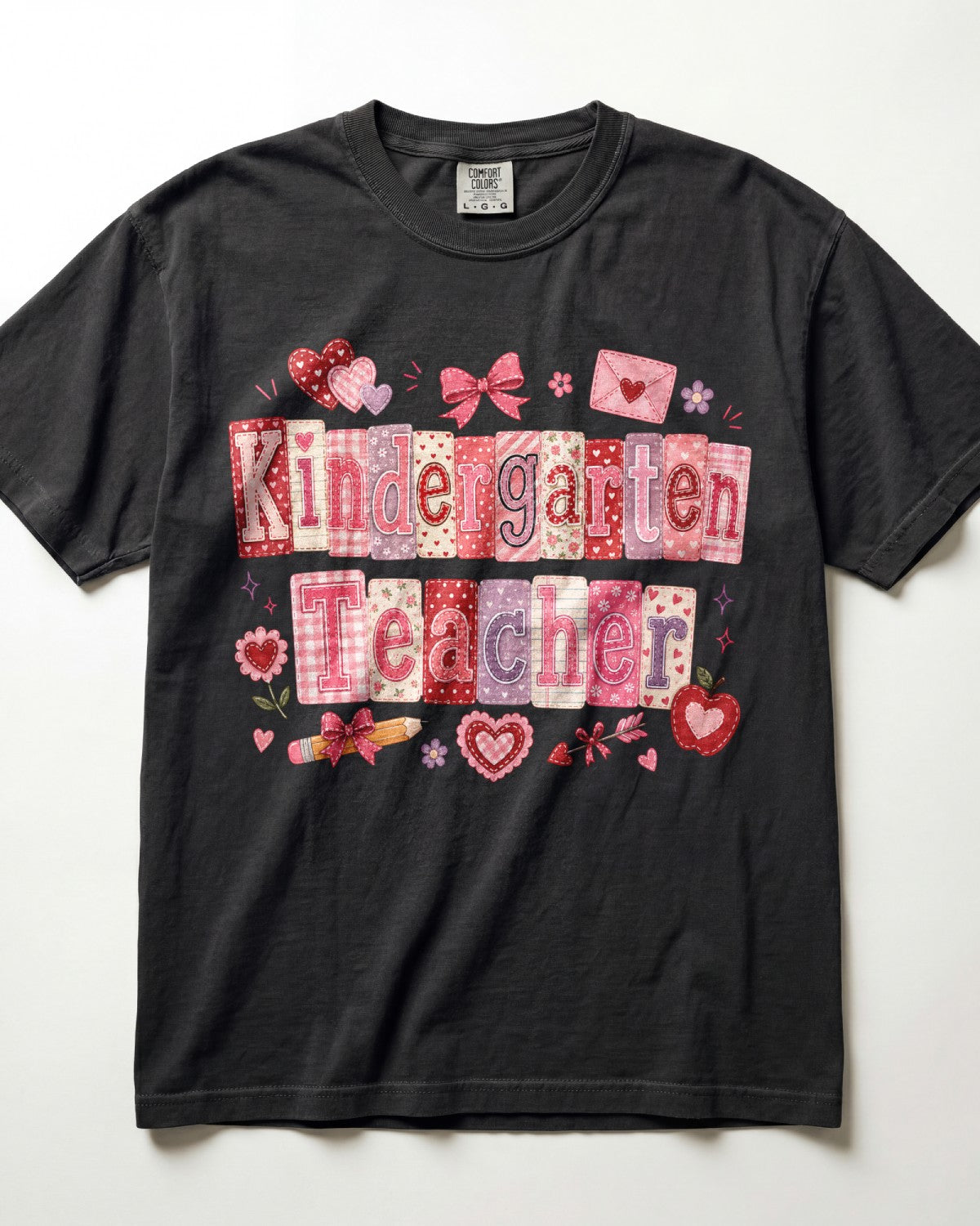 A black short-sleeve t-shirt with a 'Kindergarten Teacher' graphic made of pink and red patterned tiles, decorated with hearts, bows, and flowers, laid flat against a white background.